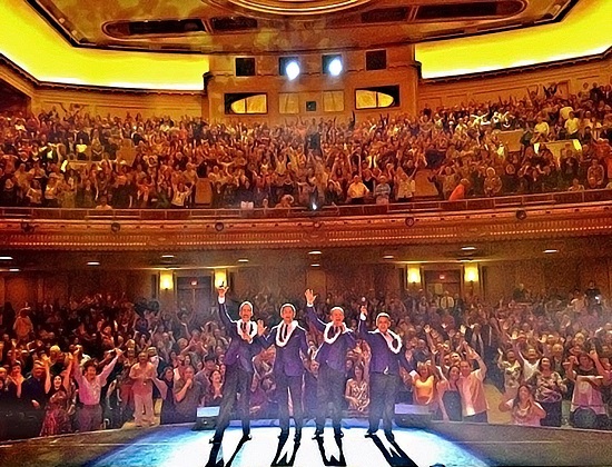 Four performers pose for a picture with a packed audience.
